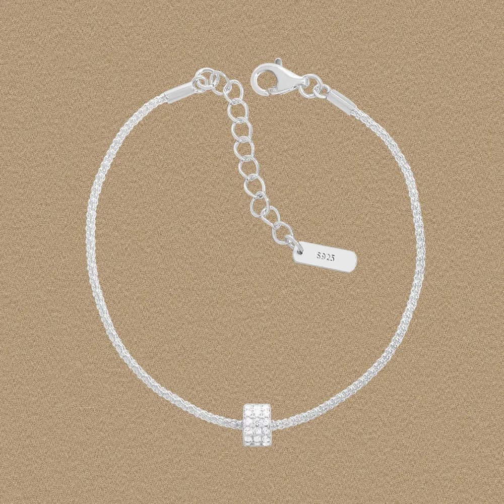Polished silver bracelet with a square pavé centerpiece on a textured background.