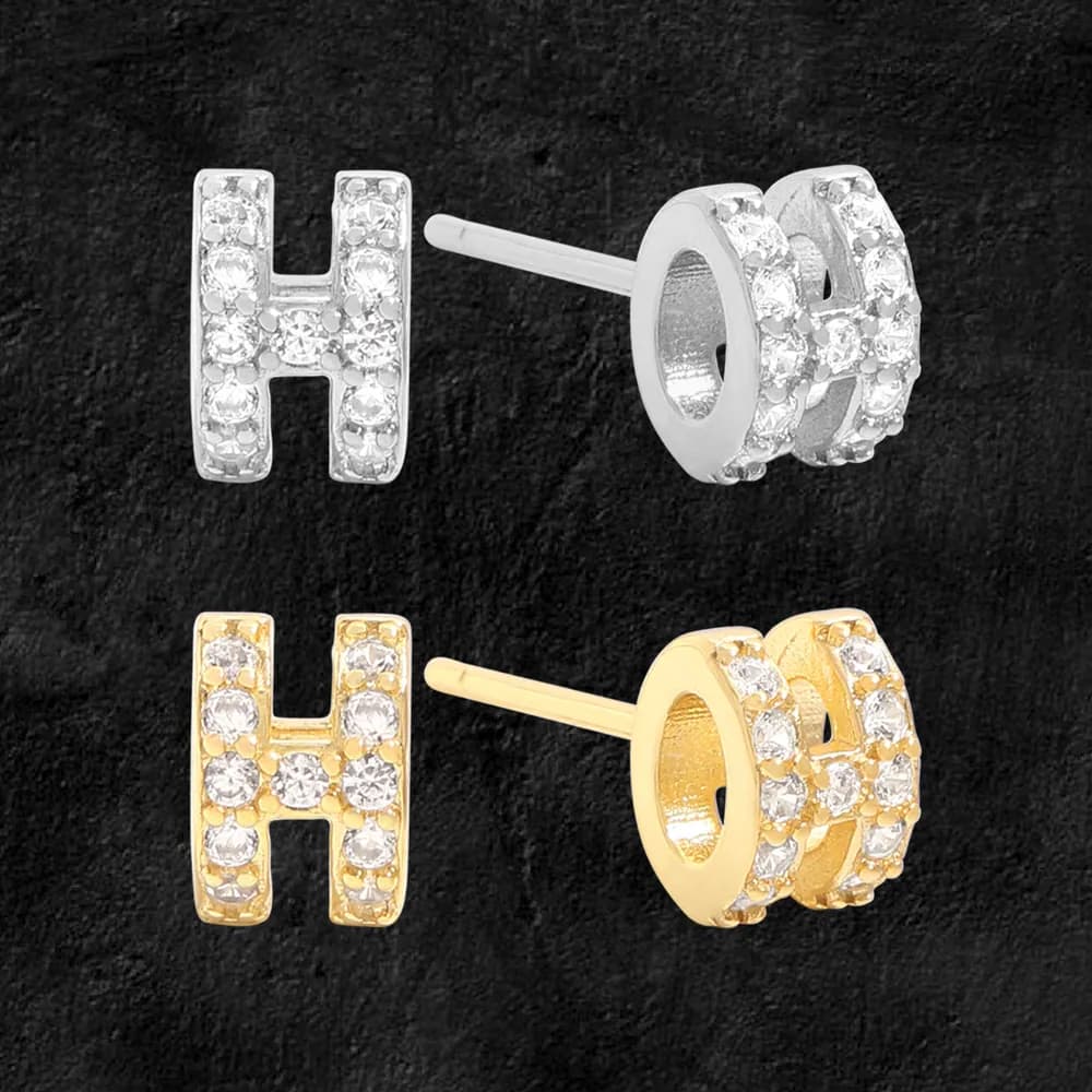 H-shaped pavé stud earrings in silver or gold-tone metal with crystal stones on a dark background.