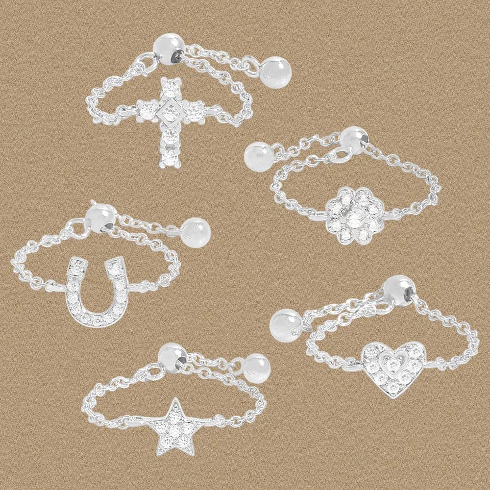 A collection of polished sterling silver charm rings with chain bands and varied charms displayed on a textured background.