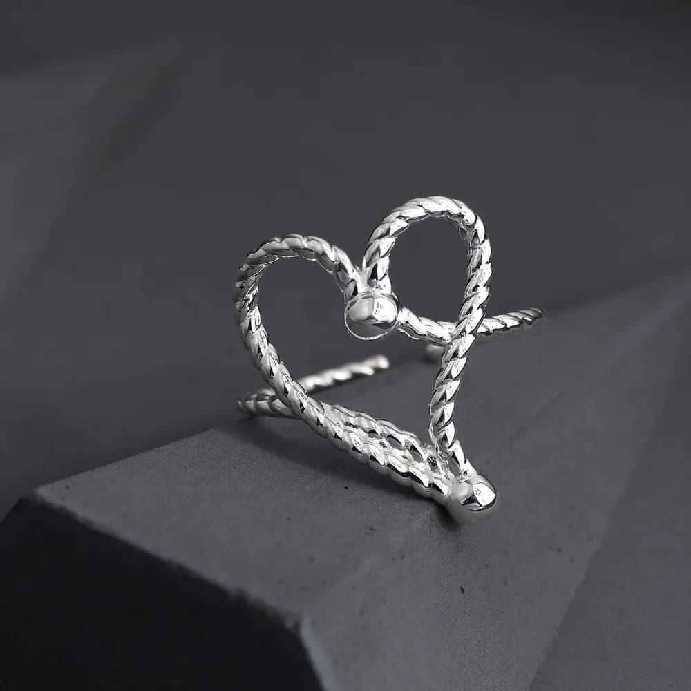 Polished sterling silver rope heart ring displayed on a dark geometric surface.