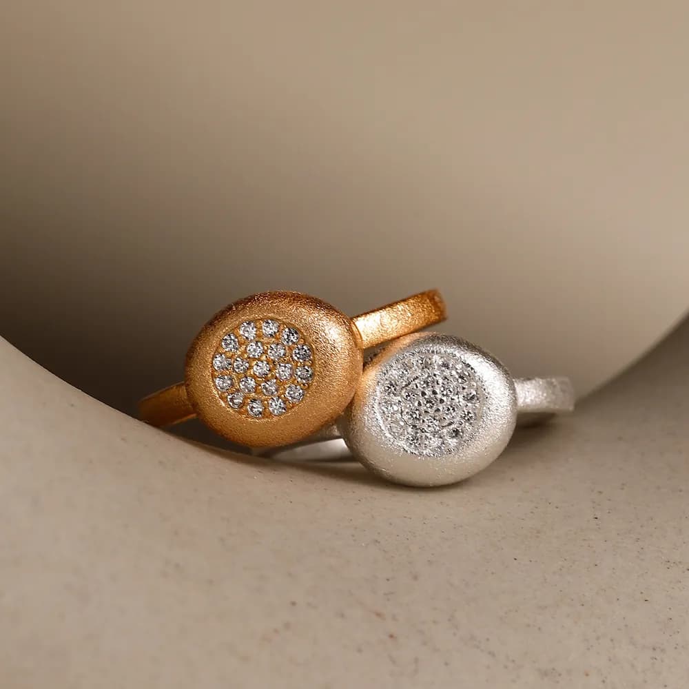 Close-up of two slim-band rings with round, pavé-studded discs in gold-tone and silver-tone finishes.