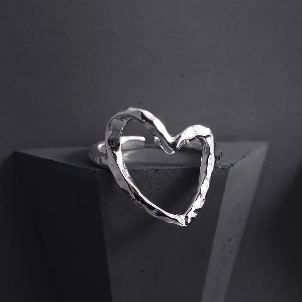 Polished silver open-heart ring resting on a dark geometric block.