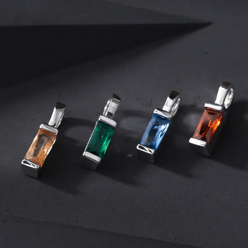 Four rectangular baguette-cut colored pendants in sterling silver on a dark surface.