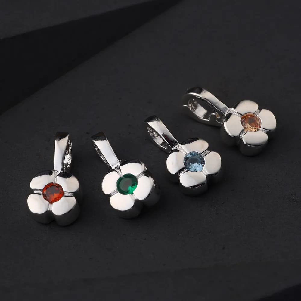 Silver flower pendants with white enamel petals and colored centers on a dark surface.