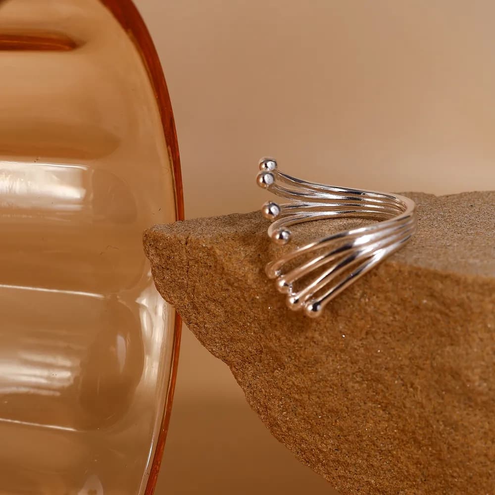 Polished sterling silver five-band open ring with small ball tips resting on a sandy surface.