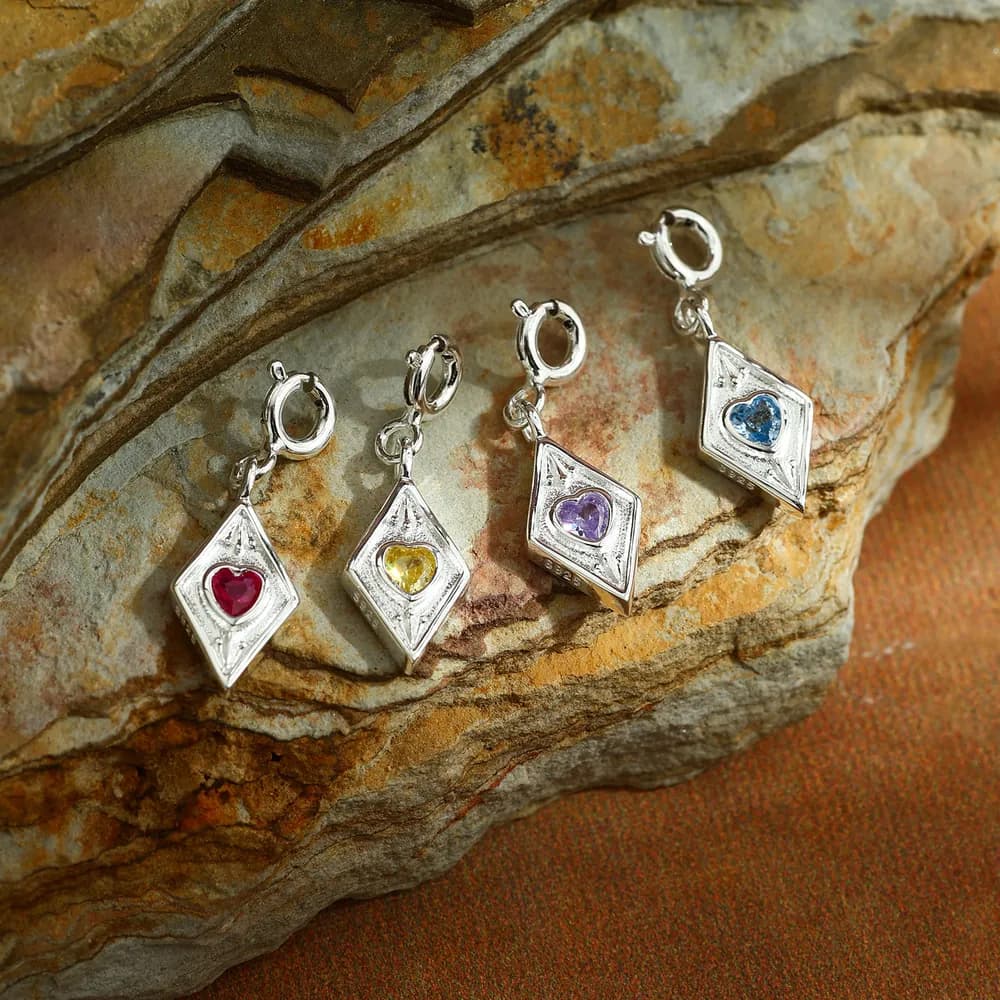 Four diamond-shaped pendants with colored heart stones arranged along a silver necklace.