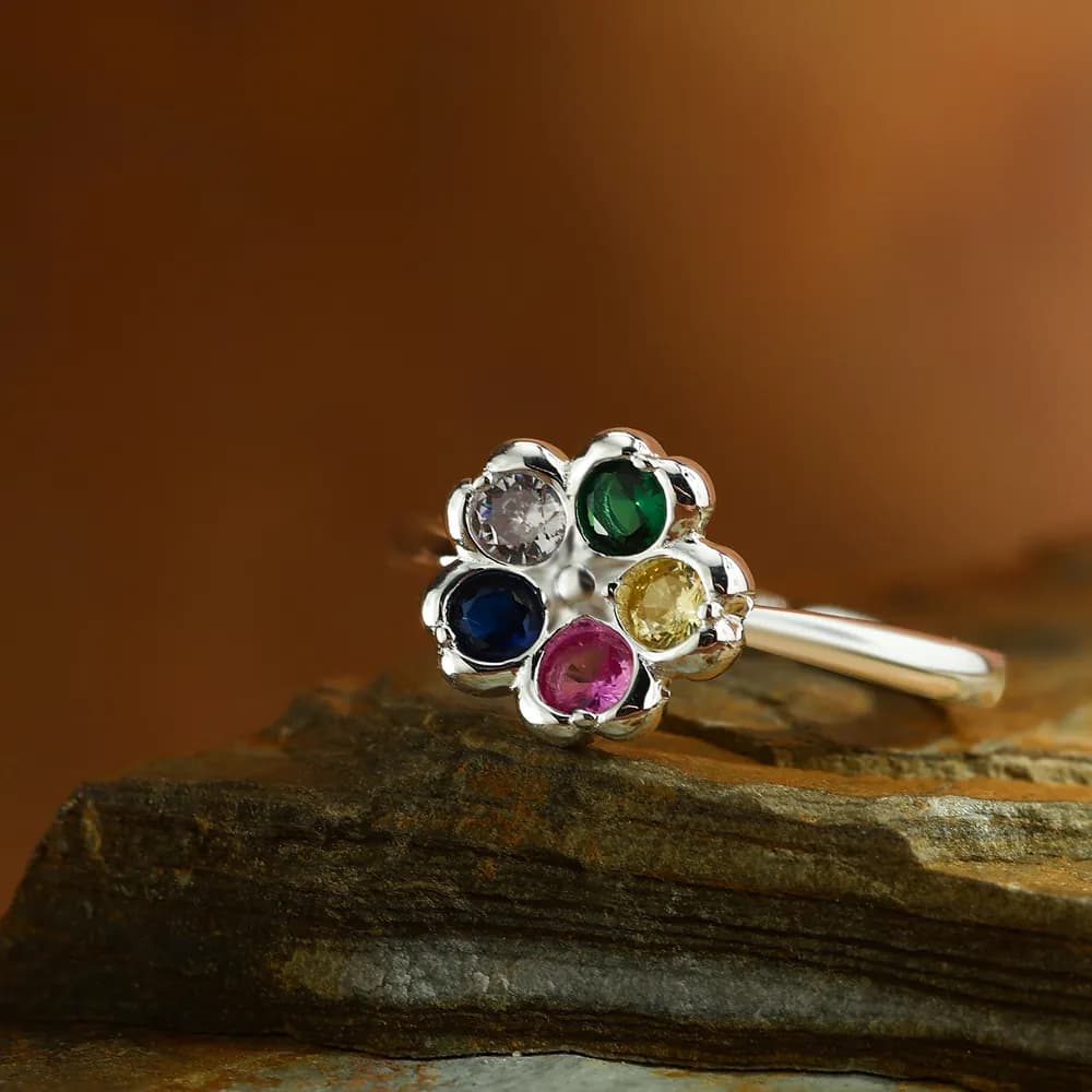Close-up of a polished silver flower ring with six colorful gemstones arranged in a petal shape.