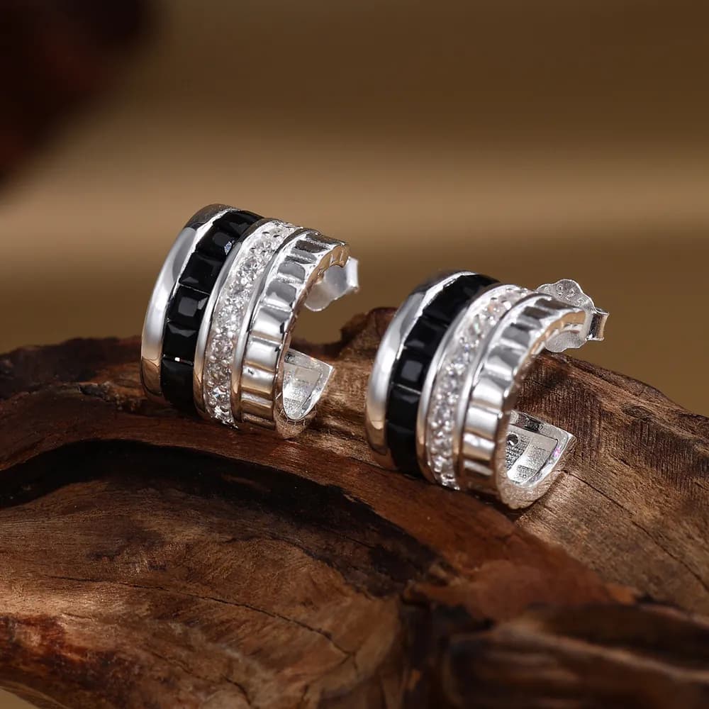 Close-up of polished sterling silver multi-band hoop earrings with black enamel and crystal pavé detailing on a wooden surface.
