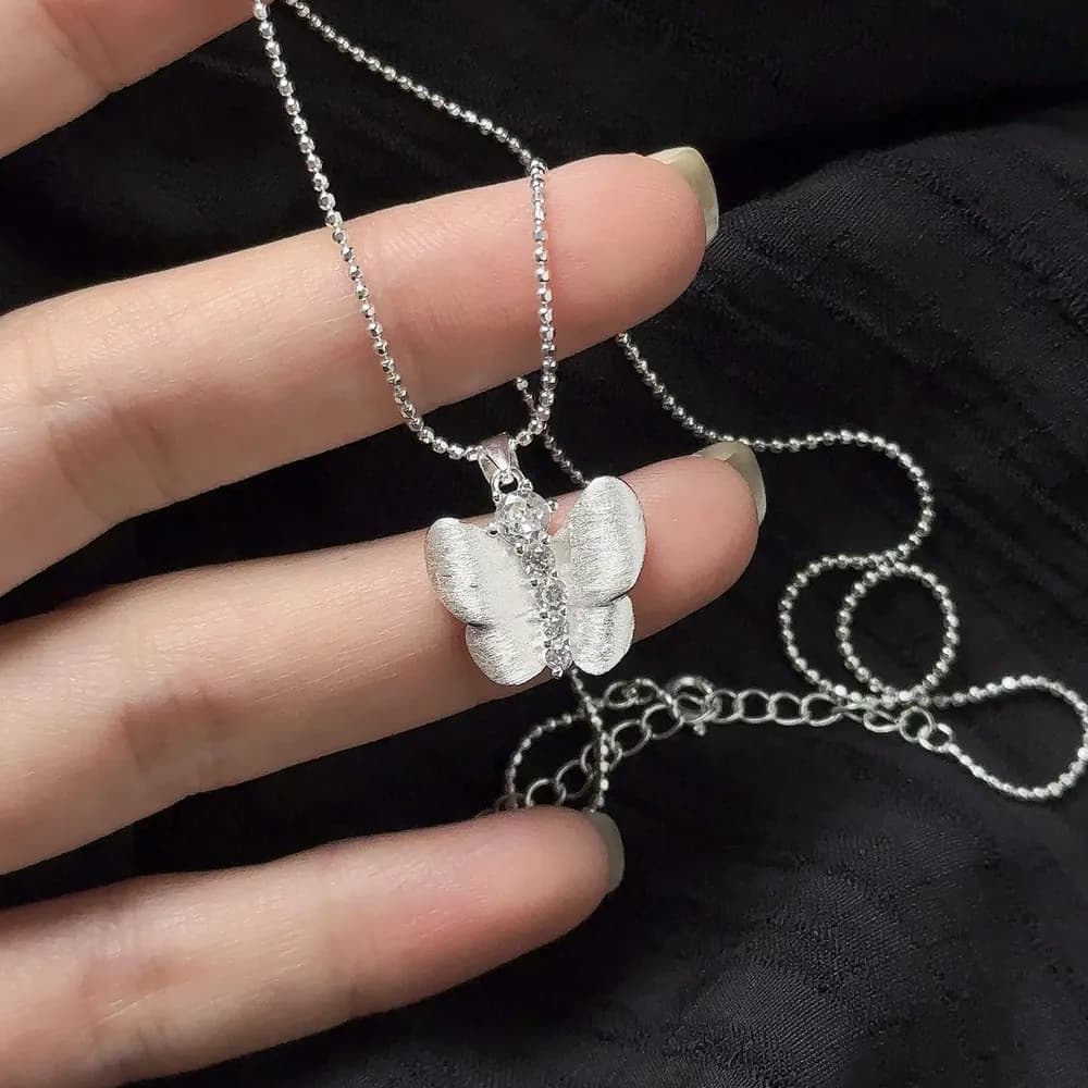 Close-up of a polished silver butterfly pendant on a beaded chain
