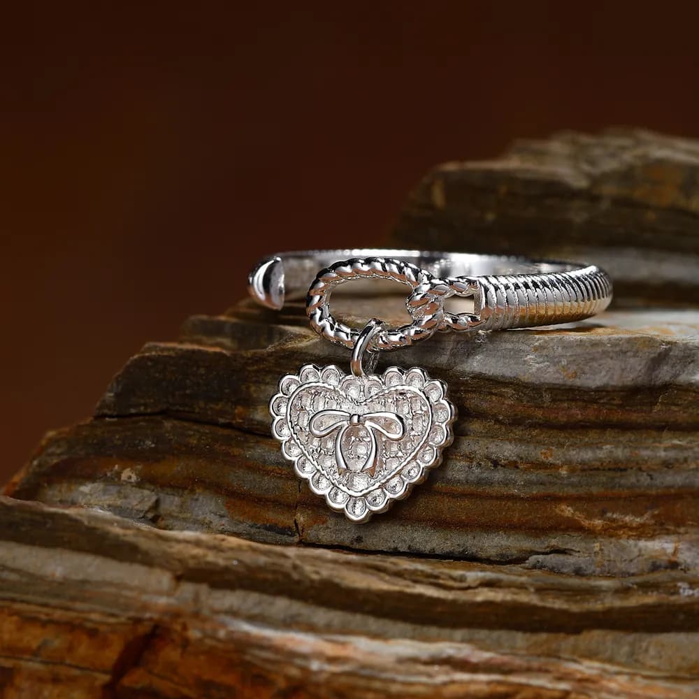 Close-up of a polished sterling silver ring with a heart-shaped scalloped charm and bow detail on a textured band.