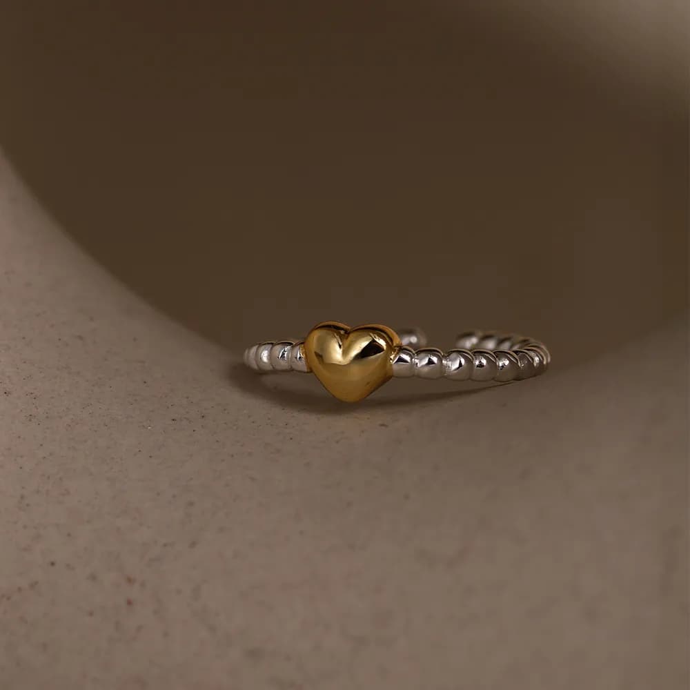 Two-tone heart ring with a gold heart centerpiece on a silver beaded band.