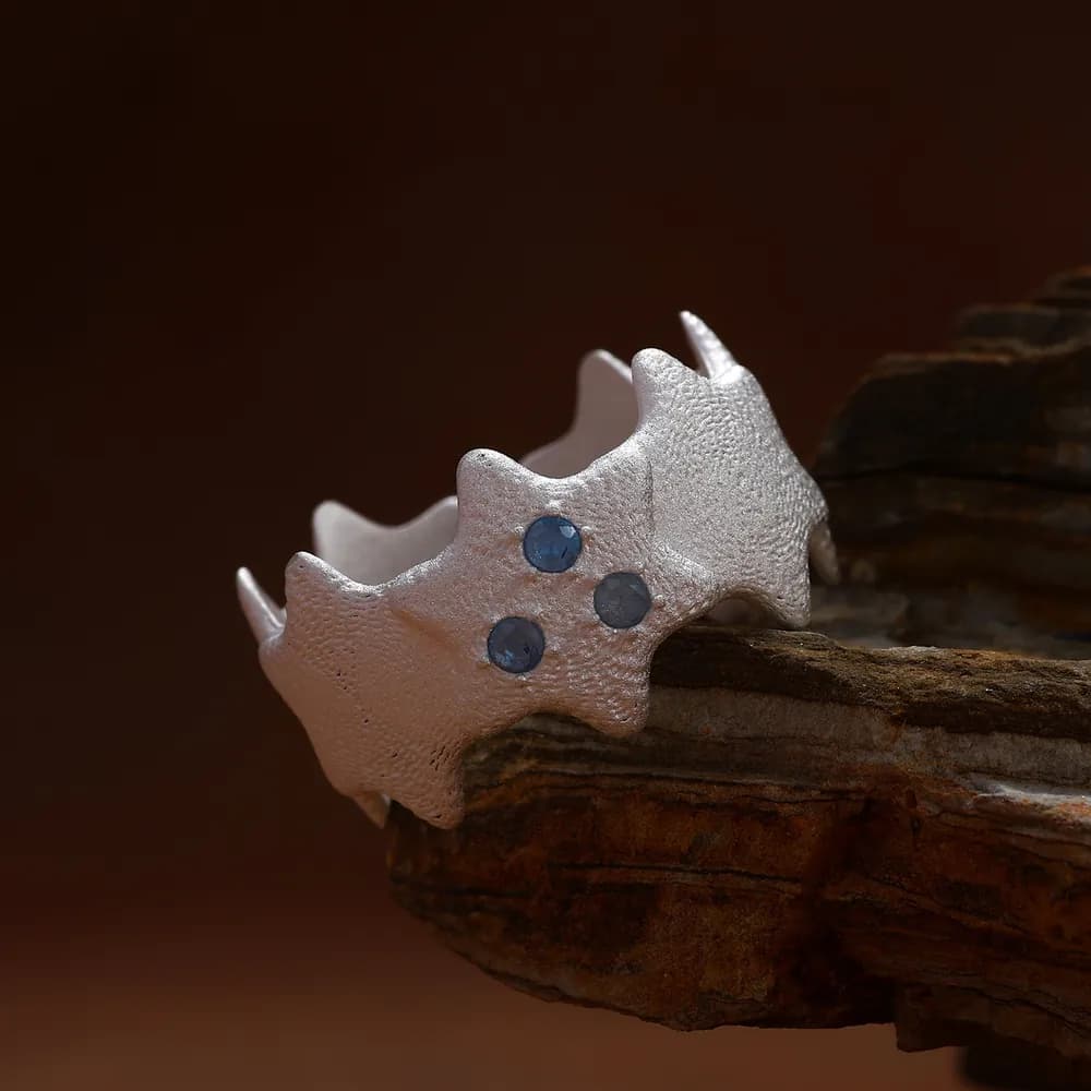 Sterling silver jagged crown ring with three blue stones resting on a wooden surface.
