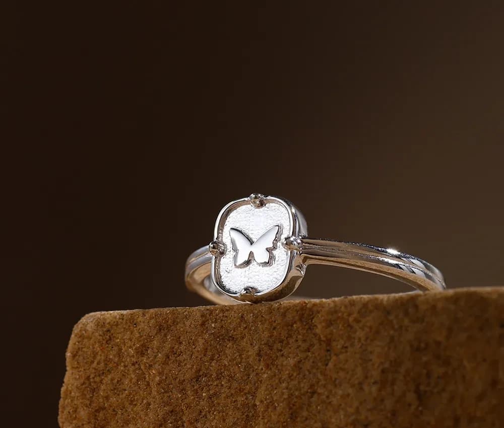 Polished sterling silver ring with butterfly cutout on a shield-shaped bezel and split band.