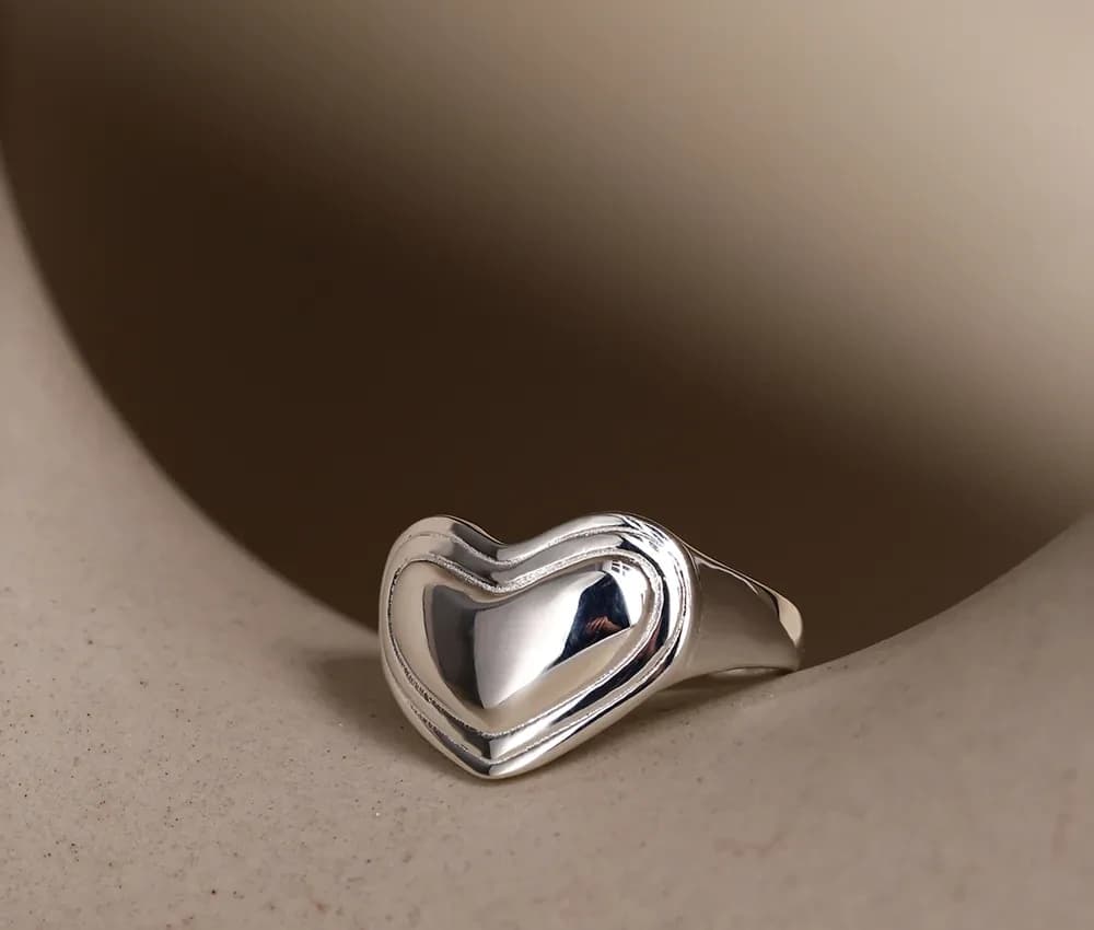 Close-up of a polished sterling silver heart-shaped ring resting on a beige surface.