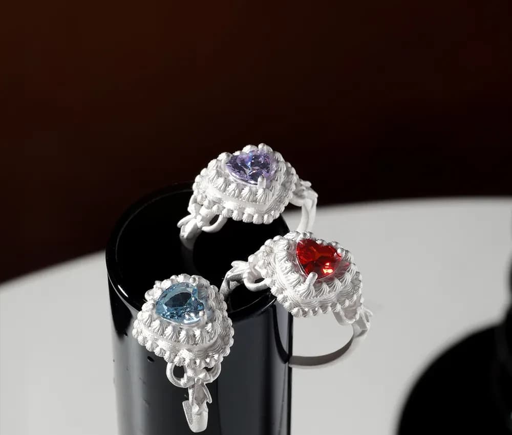 Close-up of a sterling silver ring with a heart-shaped gemstone surrounded by a braided halo on a dark display