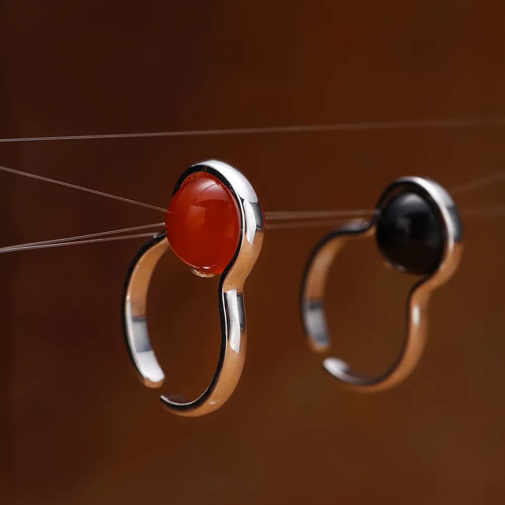 Two-tone curved hoop rings with bezel-set cabochons on top in orange-red and black.