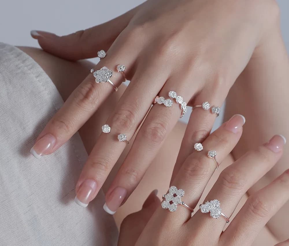 Hands wearing multiple sterling silver floral cluster rings with polished finish on different fingers.