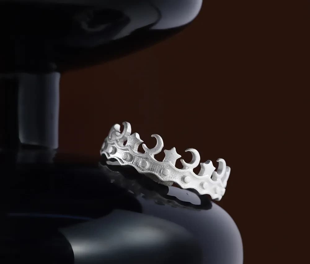 Close-up of a silver ring with scalloped crescent-shaped cutouts resting on a dark glossy surface.