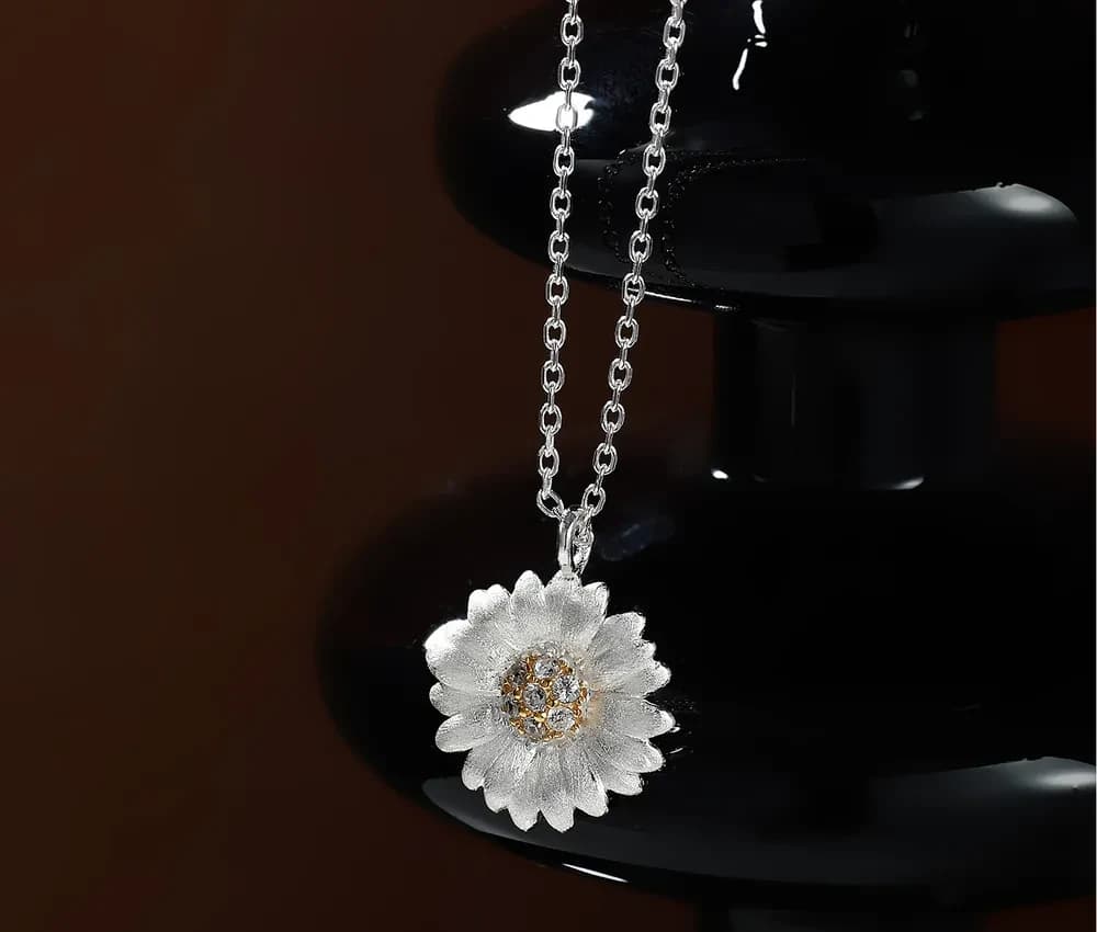 Silver flower pendant necklace with textured petals and crystal center hanging from a polished chain.