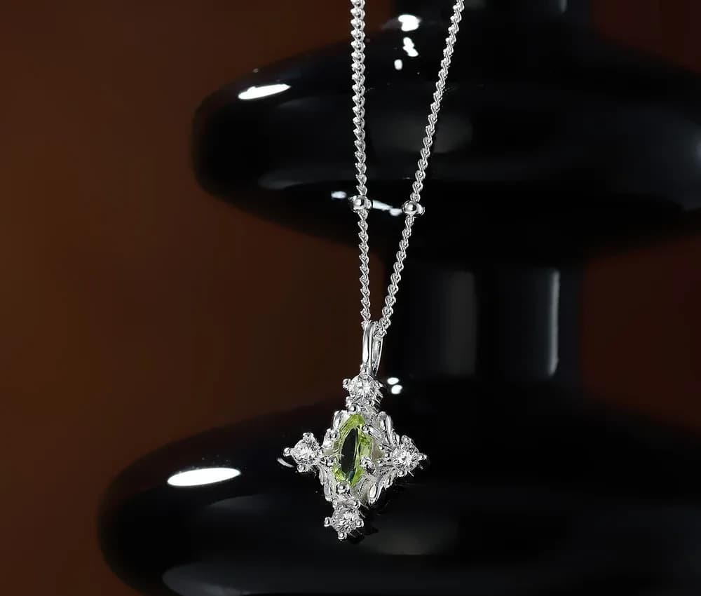 Close-up of a silver pendant necklace with a marquise green center stone and surrounding clear stones