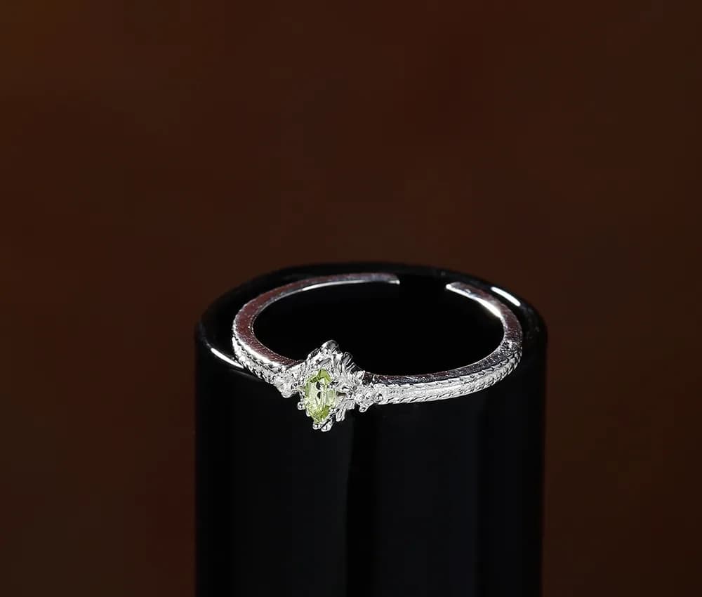 Polished sterling silver ring with a pale green peridot center sits on a dark display stand.