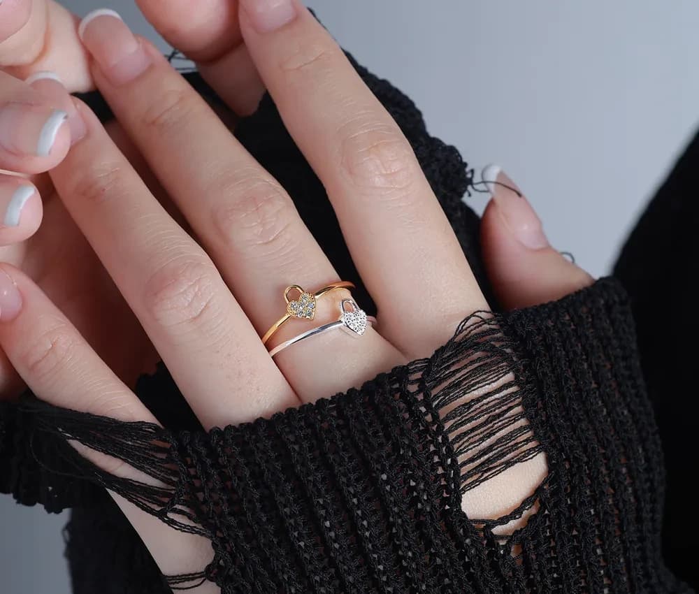Two-tone heart charm rings on a hand, showing pavé hearts on slim bands.
