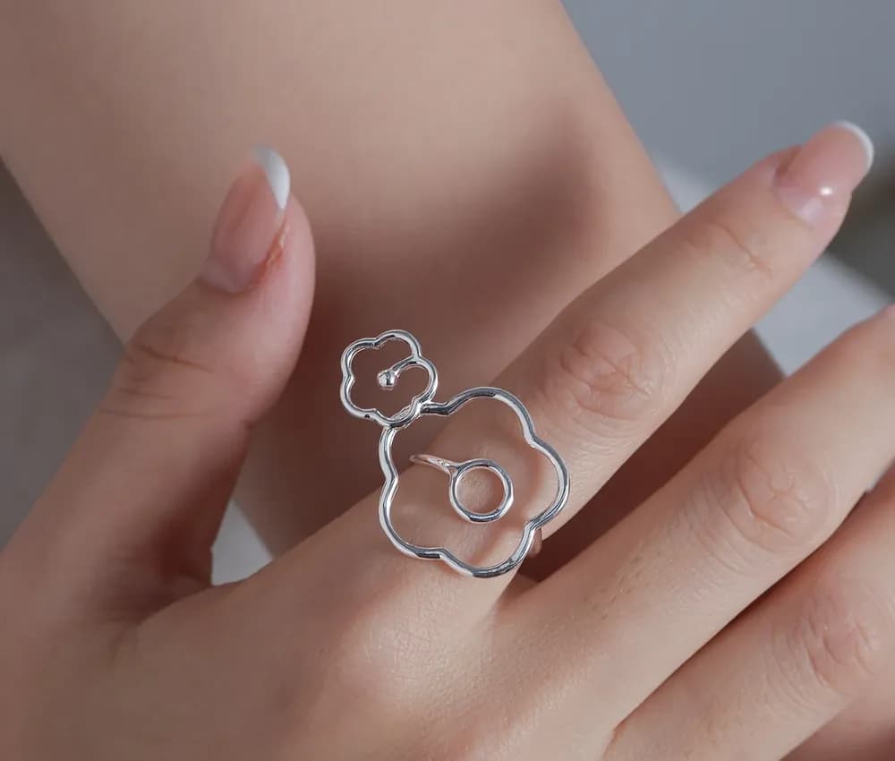 Close-up of a polished silver flower-outline ring worn on a finger.