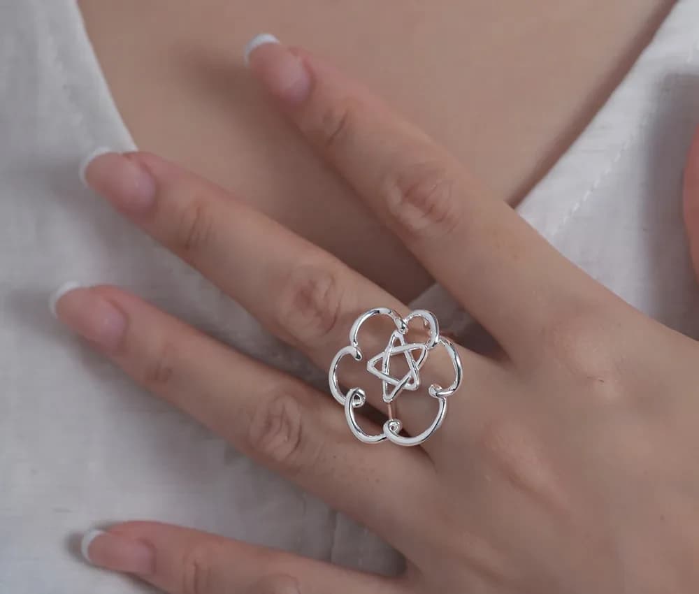 A hand wearing a polished sterling silver openwork flower ring on the ring finger.