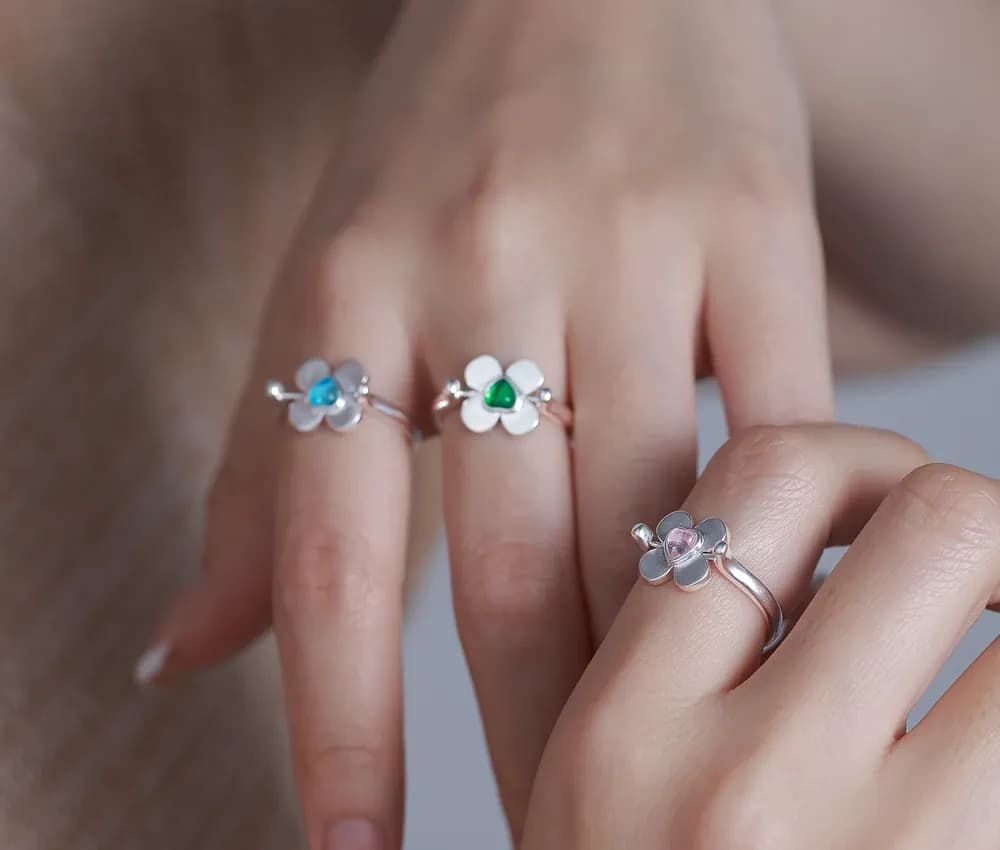 Delicate sterling silver ring with a white enamel flower and a colored gemstone center on the finger.