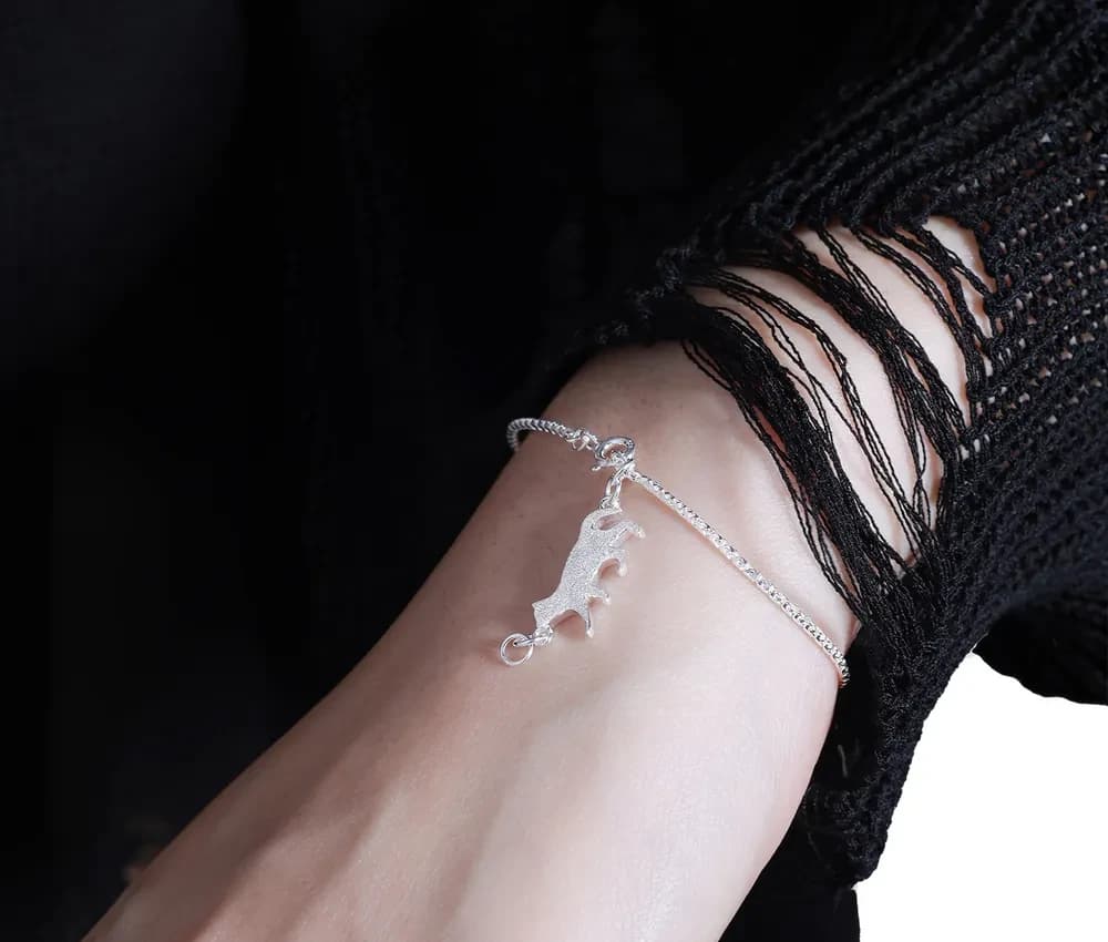 Polished sterling silver bracelet with a stegosaurus charm resting on the wrist.