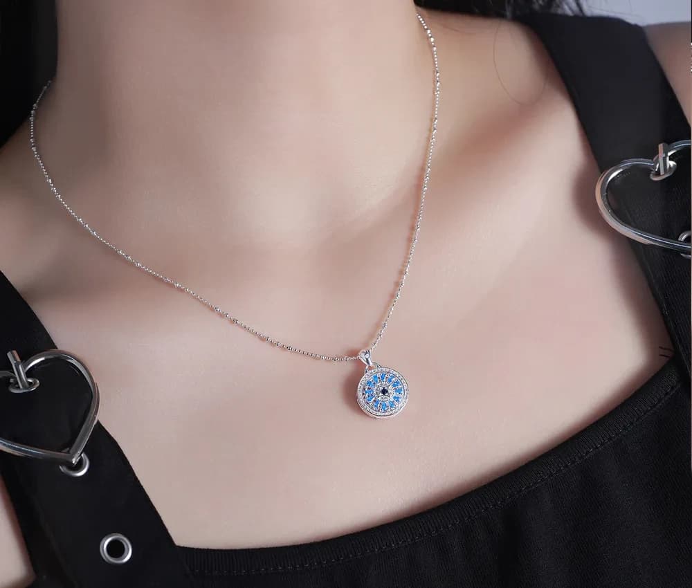 Close-up of a silver beaded chain necklace with a circular blue pavé halo pendant resting at the collarbone.