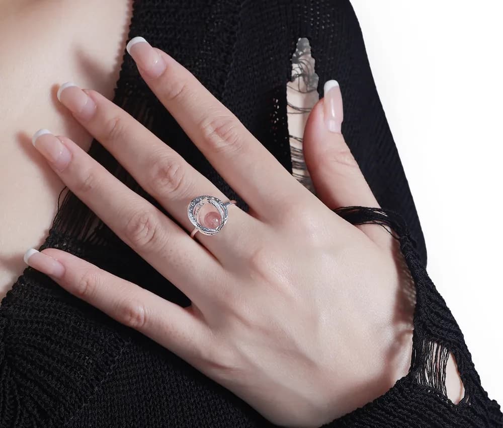 Polished sterling silver ring with a pink central cabochon and pavé halo on the model's finger.