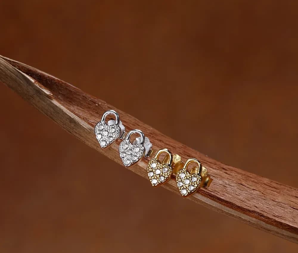 Two-tone pavé heart stud earrings in silver and gold finishes displayed on a wooden branch.