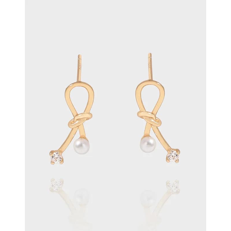 Gold-tone knot loop earrings with a pearl and small stone at the end on a light background.