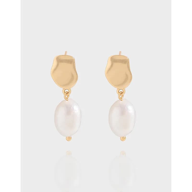Abstract gold-toned top with drop pearls on delicate earrings against a light gray background.