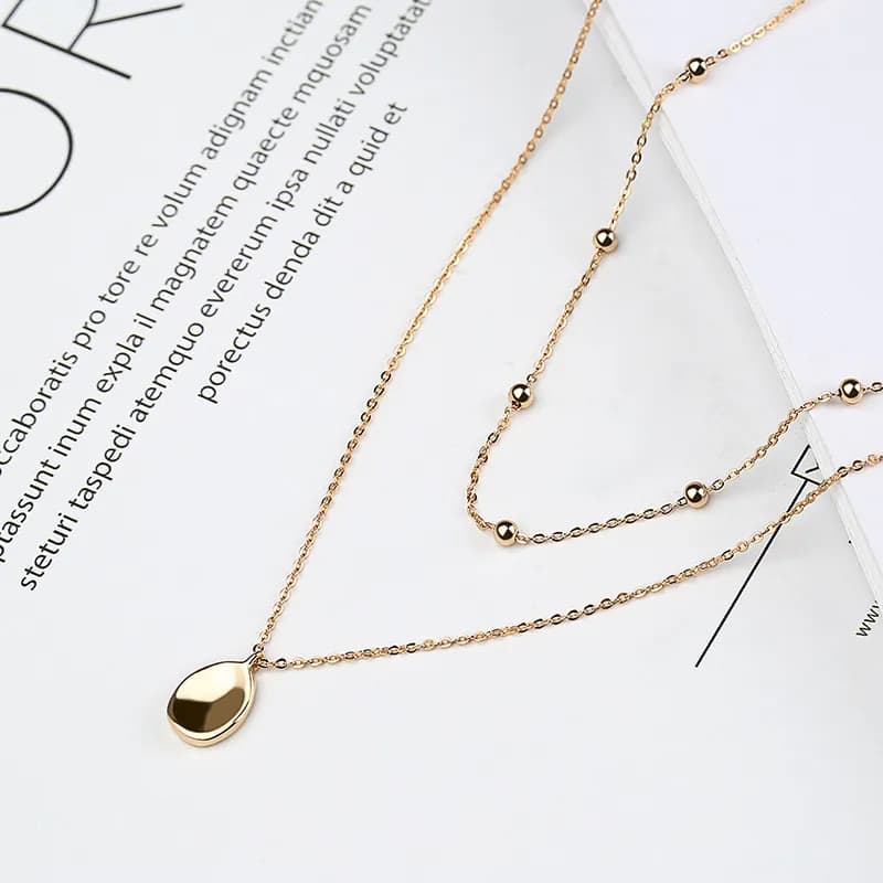 Layered sterling silver necklace with a teardrop disc pendant and beaded chain accents.