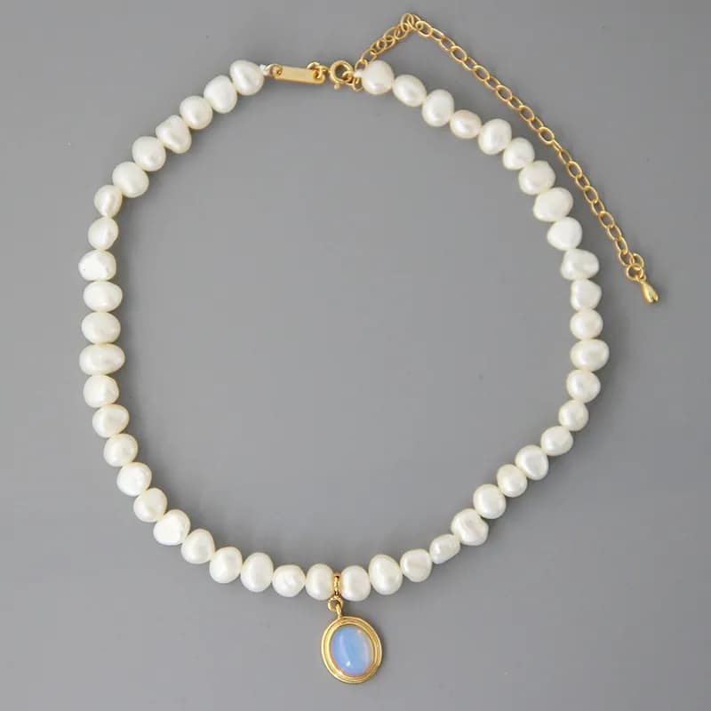 Close-up of a pearl bead necklace with a gold-tone pendant featuring a blue oval cabochon.