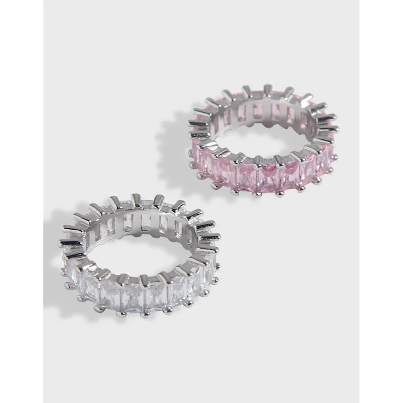 Two silver rings with evenly spaced prongs holding rectangular stones around a circular band, one with clear stones and one with pink stones.