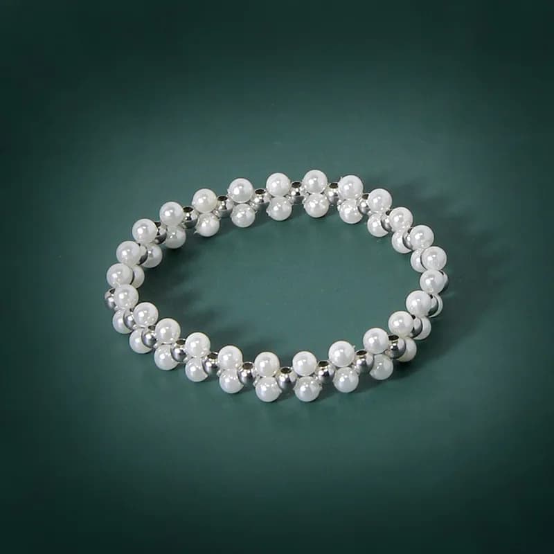 A polished sterling silver pearl bead bracelet arranged in a circular shape on a dark green background.