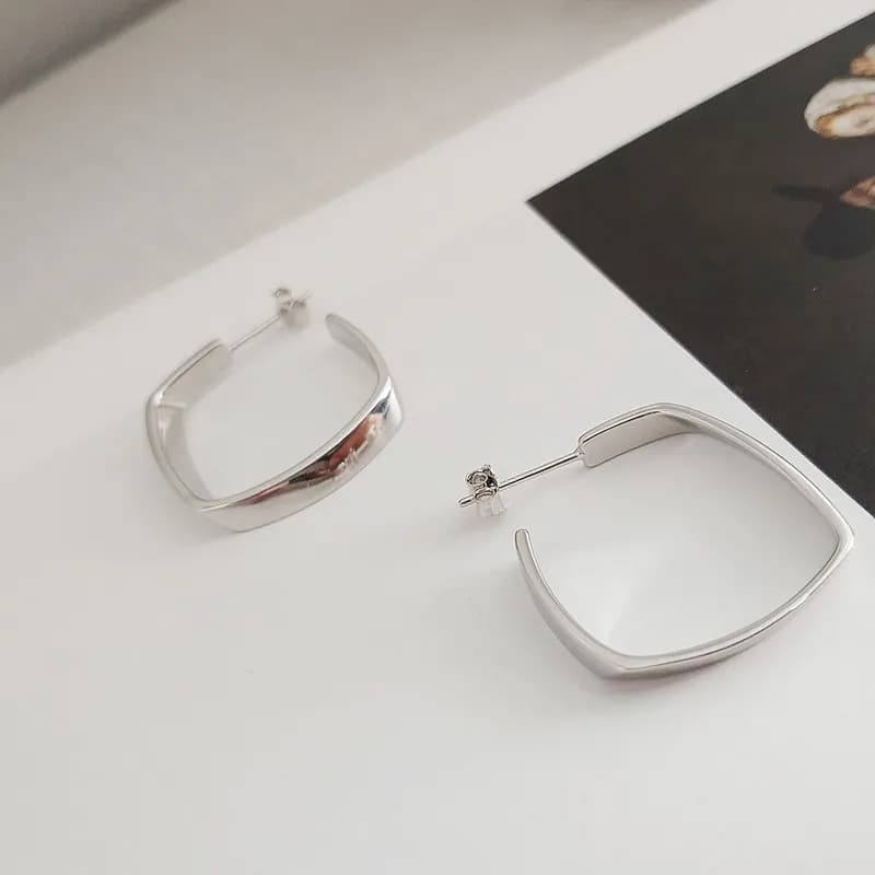 Polished curved square hoop earrings in sterling silver displayed on a white surface.