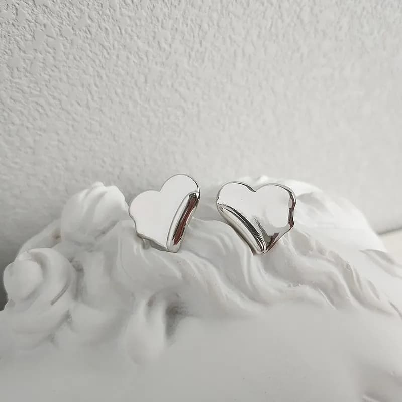 Two polished heart-shaped sterling silver stud earrings resting on a white textured surface.