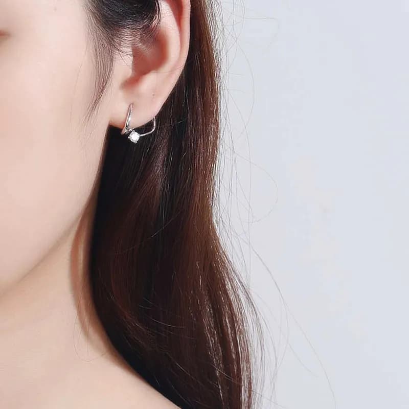 Close-up of a polished sterling silver hoop earring with a small diamond accent worn on the ear