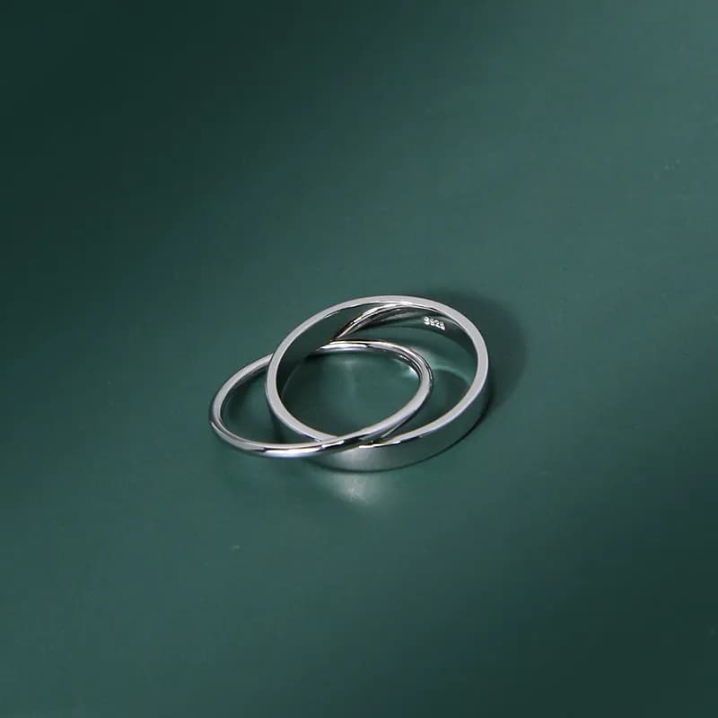 Two interlocking polished sterling silver rings resting on a dark green background.