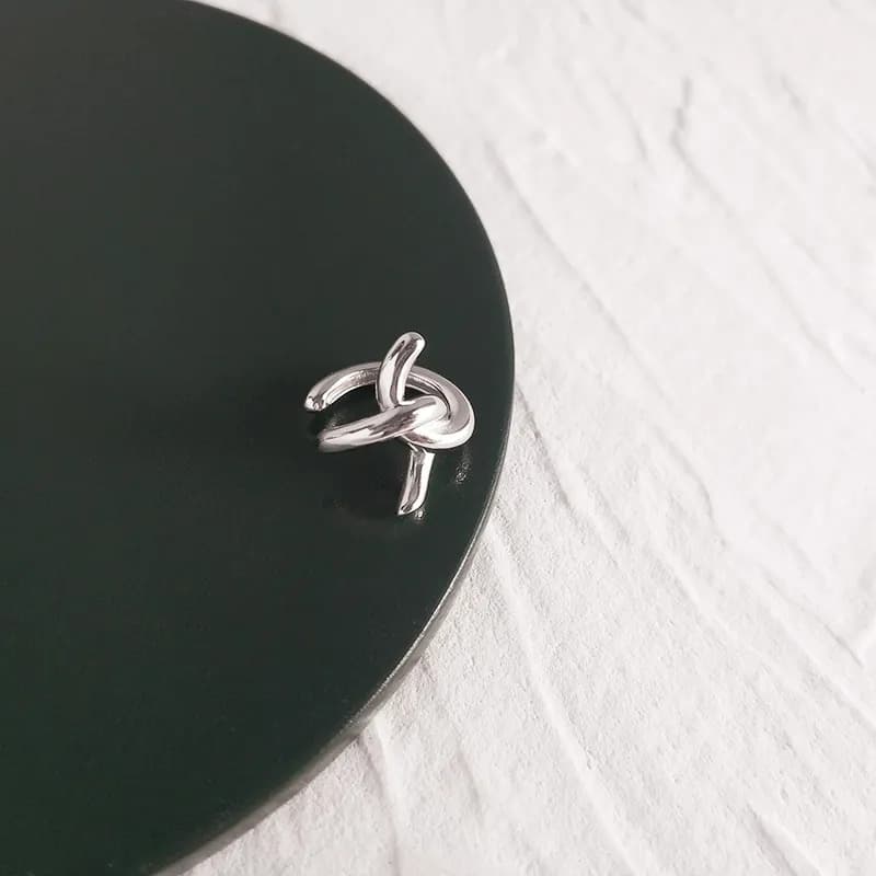 Close-up of a polished sterling silver knot earring resting on a dark circular surface.