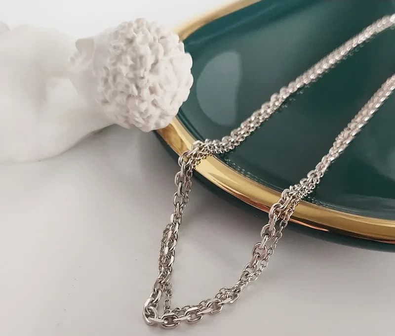 Polished sterling silver cable chain necklace draped near a green and gold plate.
