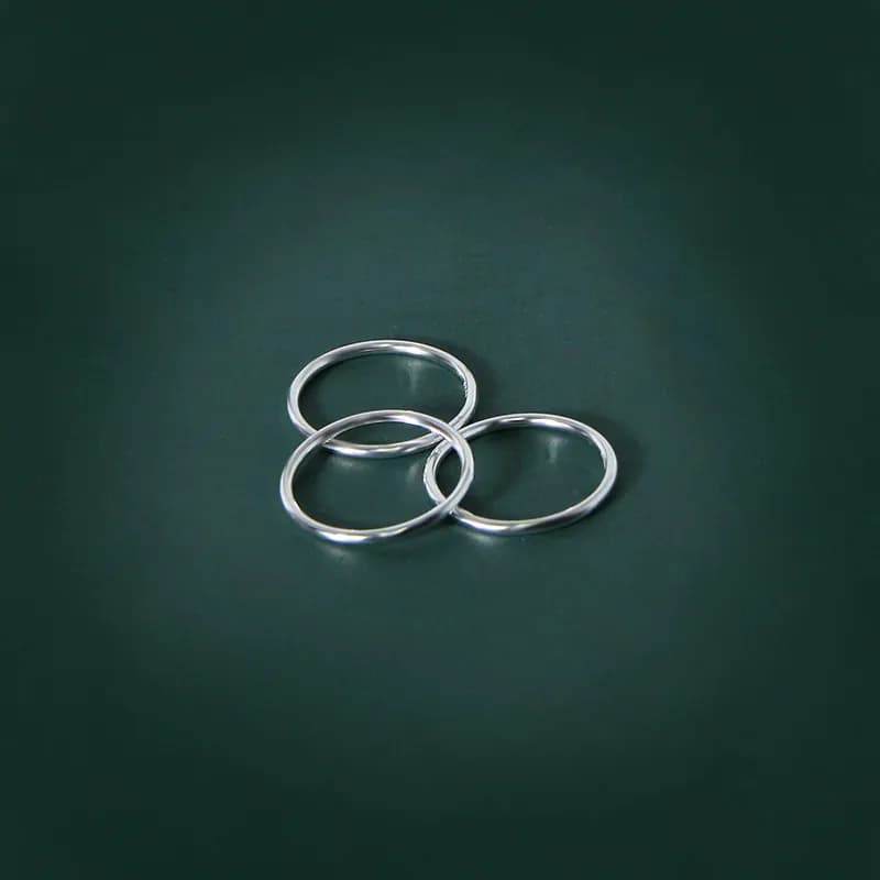 Three polished sterling silver rings loosely interlocked on a dark green surface.
