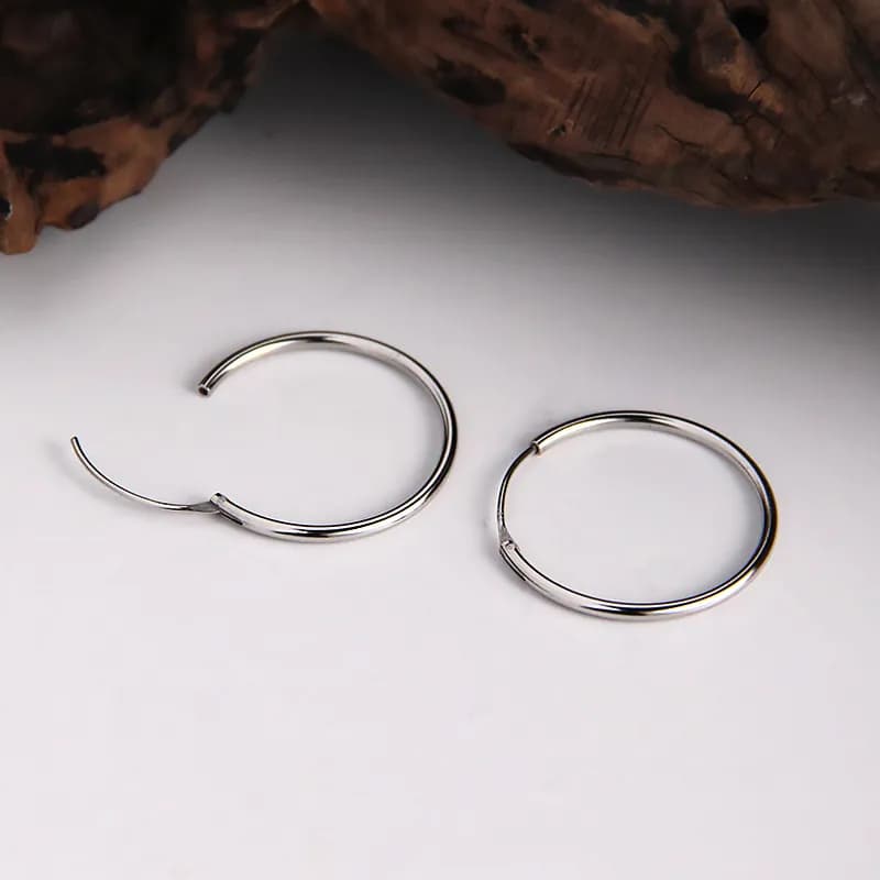 Two polished sterling silver hoop earrings on a white surface, one with an open hinge detail.