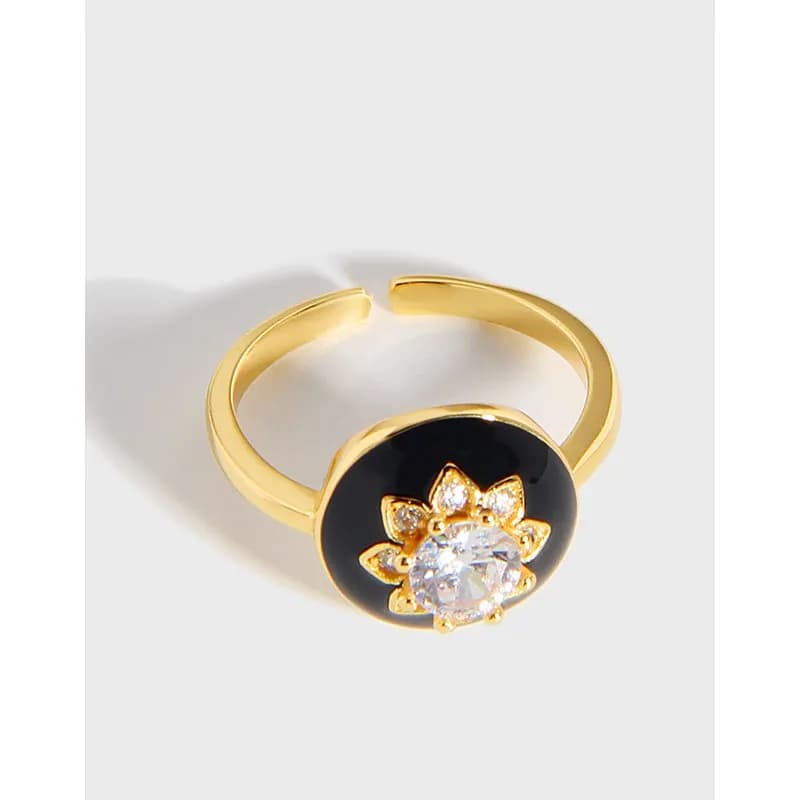 Gold-tone ring with a black enamel circle housing a central crystal and petal-shaped accents around it.