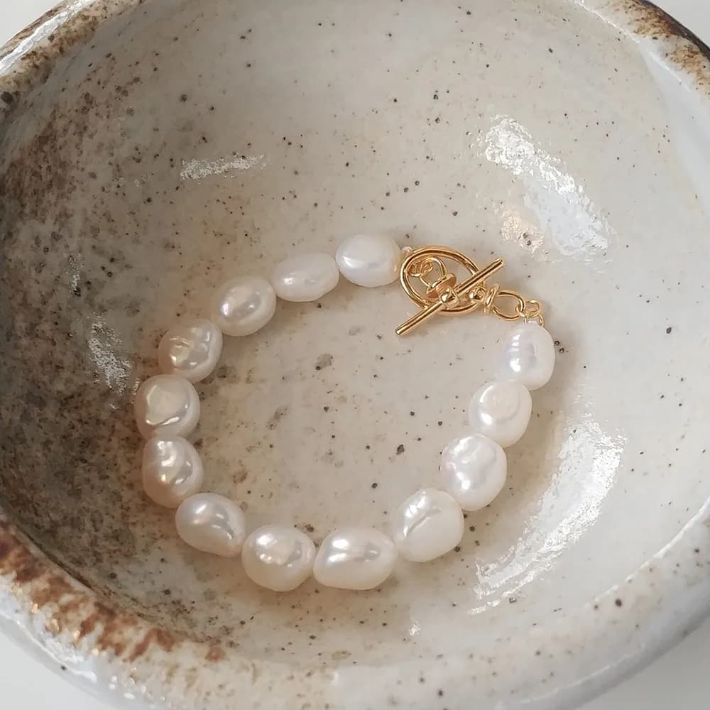 Single strand baroque pearl bracelet with a gold-tone toggle clasp laid in a shallow ceramic dish.
