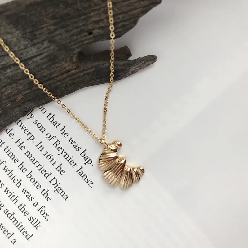 A delicate sterling silver shell-fan pendant hangs on a fine chain against a white background.